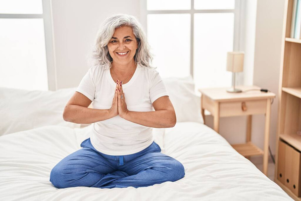 Middle age woman doing yoga exercise sitting on bed at bedroom - Foto, Bild