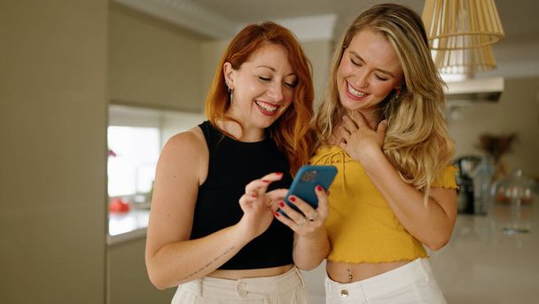 Deux femmes utilisant un smartphone debout ensemble à la maison - Photo, image