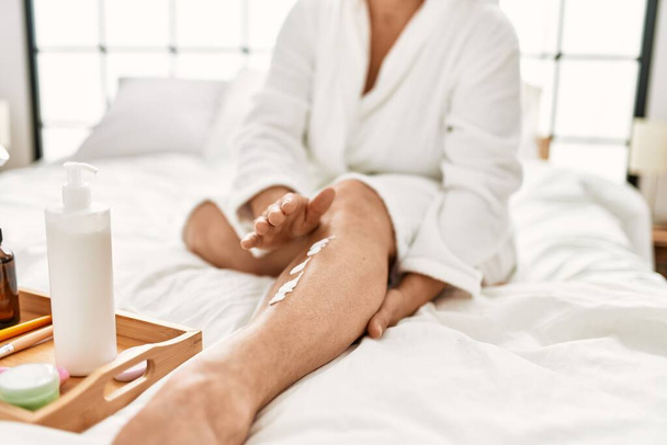 Woman caring skin legs using hydration cream sitting on the bed at bedroom. - Foto, Imagen