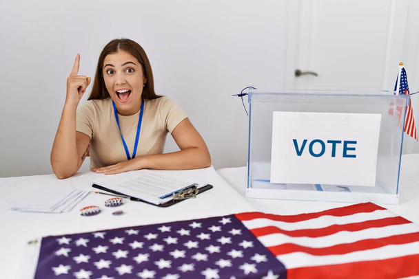 Nuori ruskeaverikkö nainen poliittisissa vaaleissa äänestyskierroksella osoittaen sormella onnistuneen idean. poistunut ja onnellinen. Numero yksi.  - Valokuva, kuva