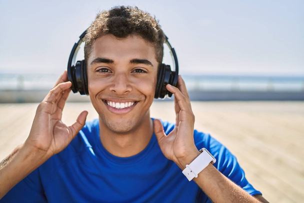 Young hispanic man training listening to music wearing headphones outdoors - Photo, Image