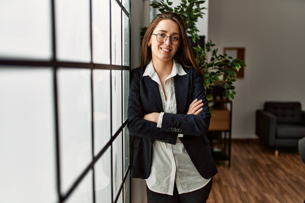 Young hispanic woman business worker standing with arms crossed gesture at office - Photo, Image