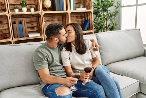 Jeune couple latin embrasser et griller avec verre de vin rouge à la maison. - Photo, image