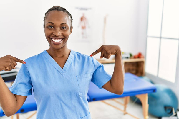 Black woman with braids working at pain recovery clinic looking confident with smile on face, pointing oneself with fingers proud and happy.  - Φωτογραφία, εικόνα