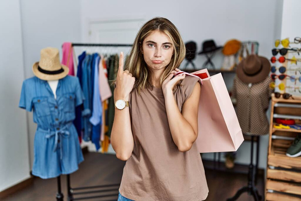 Fiatal szőke nő kezében bevásárló táskák kiskereskedelmi üzletben felmutat néz szomorú és ideges, jelezve irányt ujjak, boldogtalan és depressziós.  - Fotó, kép