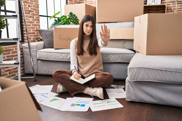 Young brunette woman moving to a new home doing finances with open hand doing stop sign with serious and confident expression, defense gesture  - Foto, Imagem