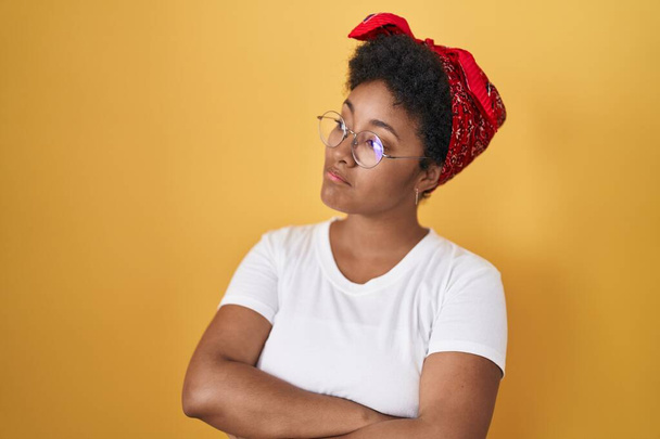 腕を組んで黄色の背景に立っている若いアフリカ系アメリカ人女性は、確信と自信を越え  - 写真・画像