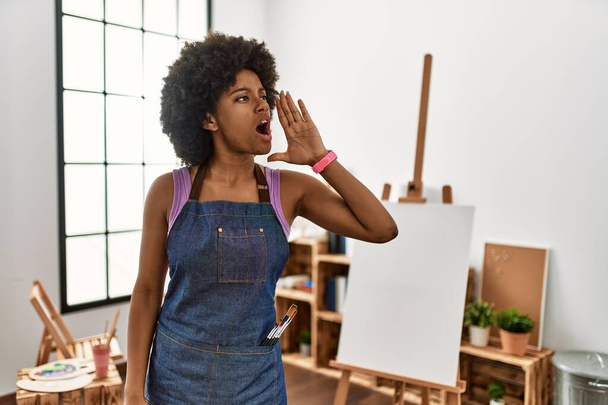 Młoda Afroamerykanka z afro-włosami w studiu artystycznym krzyczy i krzyczy głośno, by stanąć z ręką w twarz. Koncepcja komunikacji.  - Zdjęcie, obraz