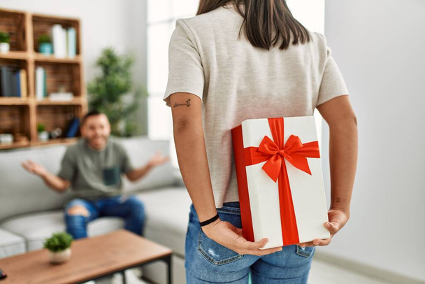 Νεαρή γυναίκα κάνει έκπληξη στο αγόρι της με δώρο γενεθλίων στο σπίτι. - Φωτογραφία, εικόνα