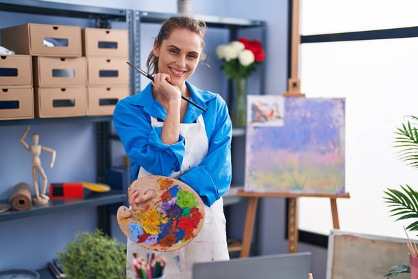 Young woman artist holding paintbrush and palette at art studio - Fotografie, Obrázek