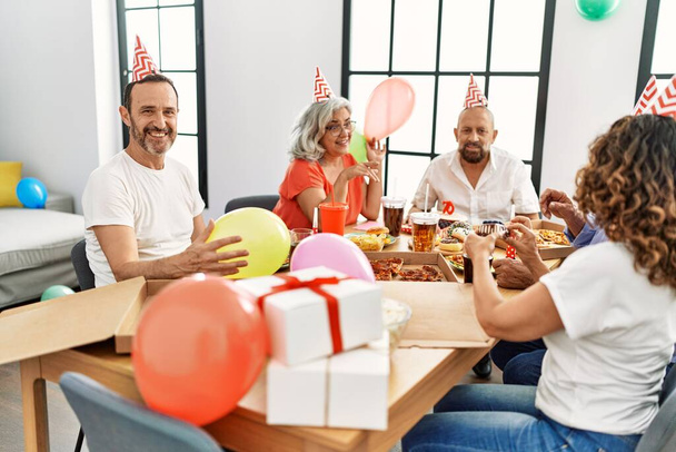 Группа друзей средних лет с улыбкой празднуют день рождения дома. - Фото, изображение