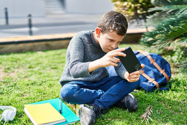 Blond child playing video game sitting on grass at park - Photo, Image