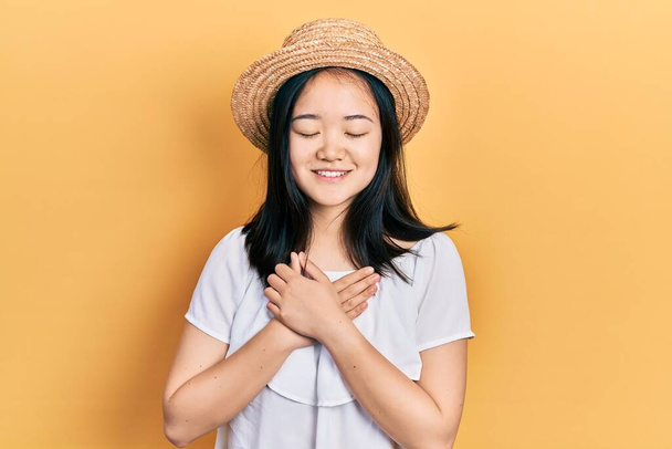 Young chinese girl wearing summer hat smiling with hands on chest with closed eyes and grateful gesture on face. health concept.  - Foto, immagini