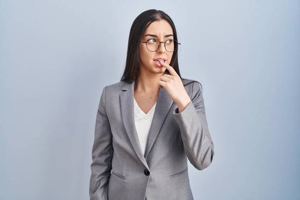 Hispanic business woman wearing glasses looking stressed and nervous with hands on mouth biting nails. anxiety problem.  - Foto, imagen