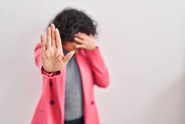 Hispanic woman with curly hair standing over isolated background covering eyes with hands and doing stop gesture with sad and fear expression. embarrassed and negative concept.  - Foto, immagini