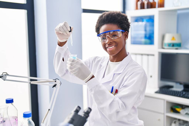 Mujer afroamericana vistiendo uniforme científico midiendo líquido en laboratorio - Foto, imagen