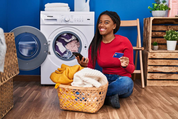 Afroamerykanka używa smartfona i karty kredytowej do prania ubrań w pralni - Zdjęcie, obraz