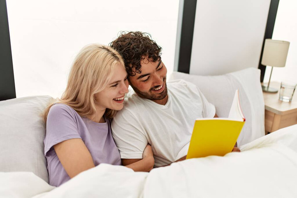 Young beautiful couple reading book lying in bed at home. - Foto, afbeelding