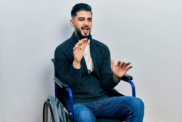 Handsome man with beard sitting on wheelchair disgusted expression, displeased and fearful doing disgust face because aversion reaction. with hands raised  - Zdjęcie, obraz