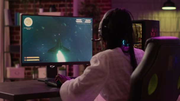 Over shoulder view of african american gamer girl playing space shooter simulation using pc gaming setup enjoying free time at home. Woman streaming online action game multiplayer competition. - Footage, Video
