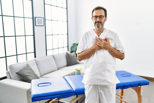 Middle age physiotherapy man working at home smiling with hands on chest with closed eyes and grateful gesture on face. health concept.  - Foto, immagini