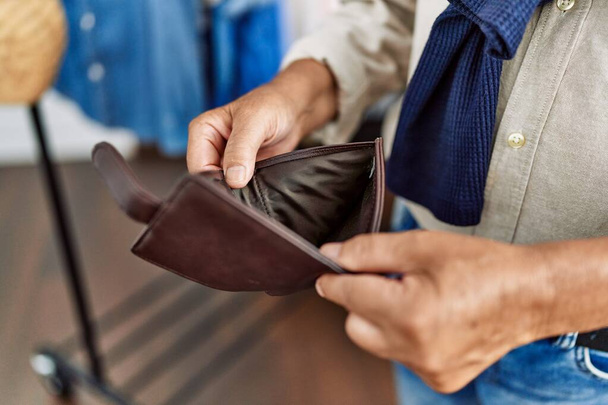 Starší šedovlasý muž ukazující prázdnou peněženku v obchodě s oblečením - Fotografie, Obrázek