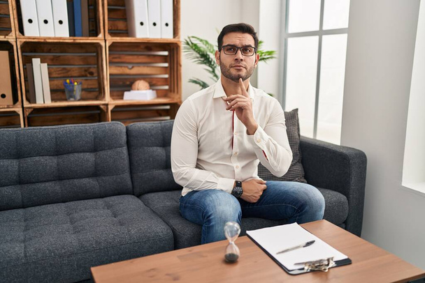 Young hispanic man with beard working at consultation office thinking concentrated about doubt with finger on chin and looking up wondering  - Foto, Bild
