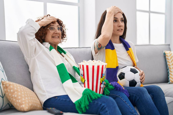 Hispanic mother and daughter watching football supporting team stressed and frustrated with hand on head, surprised and angry face  - Valokuva, kuva