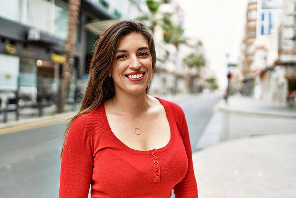 Молодая латиноамериканка улыбается счастливо стоя в городе. - Фото, изображение