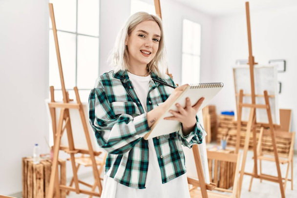 Joven estudiante artista sonriendo feliz pintura en el estudio de arte. - Foto, Imagen