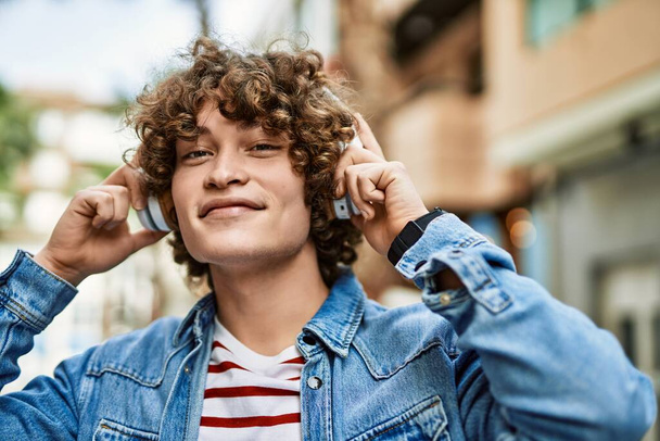 Jonge Spaanse man luistert naar muziek met een koptelefoon in de stad. - Foto, afbeelding