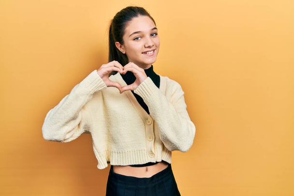 Young brunette girl wearing casual yellow jacket smiling in love doing heart symbol shape with hands. romantic concept.  - Φωτογραφία, εικόνα
