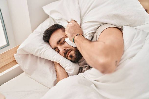 Junger hispanischer Mann liegt auf Bett und leidet unter Schlaflosigkeit wegen Lärm im Schlafzimmer - Foto, Bild
