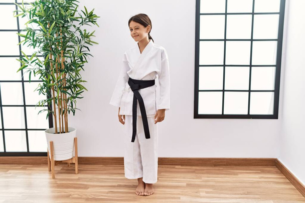 Young hispanic girl wearing karate kimono and black belt winking looking at the camera with sexy expression, cheerful and happy face.  - Foto, immagini