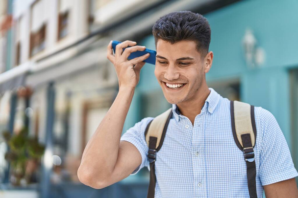 Young hispanic man student listening audio message by smartphone at street - Zdjęcie, obraz