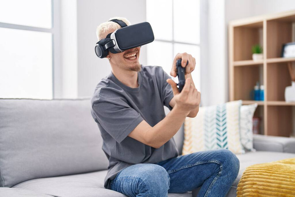 Young caucasian man playing video game using virtual reality glasses at home - Fotó, kép