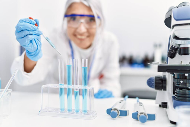 Femme aux cheveux gris d'âge moyen portant un uniforme de scientifique utilisant une pipette au laboratoire - Photo, image