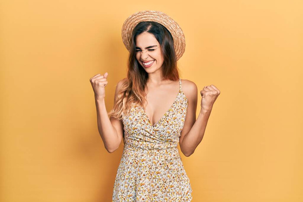 Chica hispana joven con sombrero de verano muy feliz y emocionada haciendo gesto ganador con los brazos levantados, sonriendo y gritando por el éxito. concepto de celebración.  - Foto, imagen