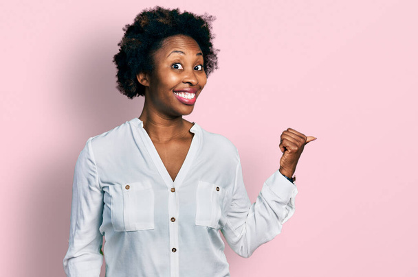 African american woman with afro hair wearing casual white t shirt smiling with happy face looking and pointing to the side with thumb up.  - Foto, immagini