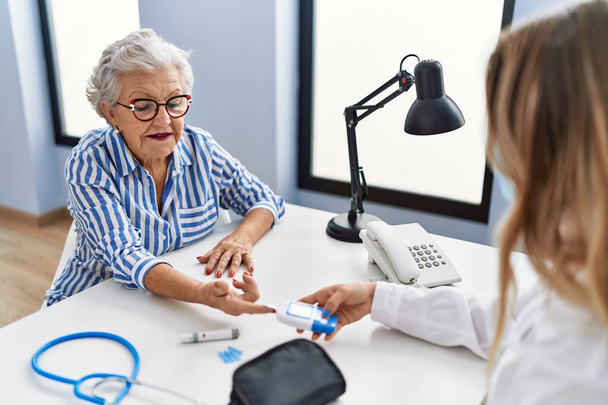 Oudere grijs-harige vrouw patiënt met medisch consult meten glucose in de kliniek - Foto, afbeelding