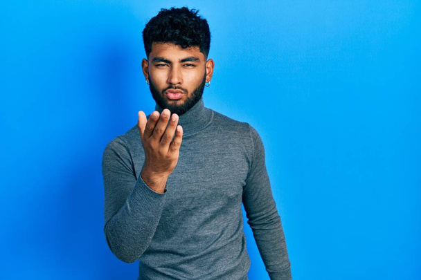 Arab man with beard wearing turtleneck sweater looking at the camera blowing a kiss with hand on air being lovely and sexy. love expression.  - Foto, immagini