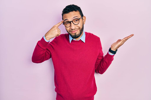 Hispanic man with beard wearing business shirt and glasses confused and annoyed with open palm showing copy space and pointing finger to forehead. think about it.  - Foto, Imagem