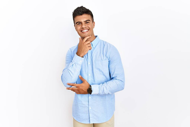 Nuori latinomies yllään liike-paita seisoo yli eristetty tausta näyttää luottavainen kameran hymyillen ristissä kädet ja käsi nostetaan leuka. positiivinen ajattelu.  - Valokuva, kuva