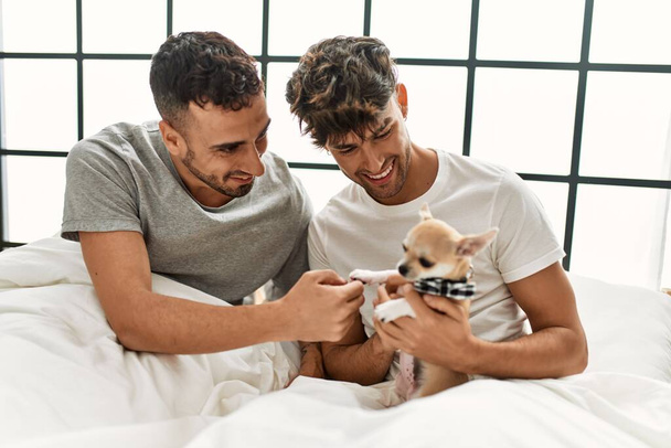 Twee Spaanse mannen paar zitten op bed met chihuahua in de slaapkamer - Foto, afbeelding