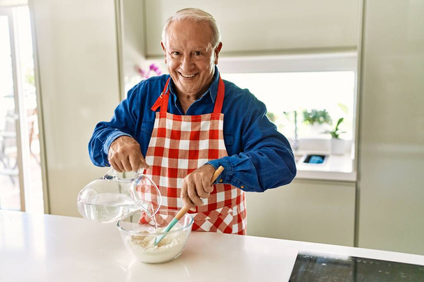 Старший улыбается, уверенно готовит тесто на кухне - Фото, изображение