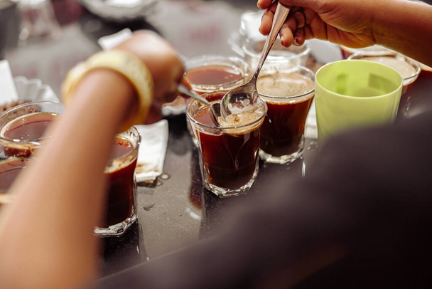 Cropped photo of cup taster man with spoons in hands tasting degustation coffee. Quality test - 写真・画像