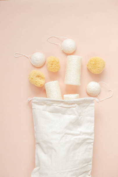 Doğal konyak süngerleri, banyo lifleri ve bej renkli arka planda bej bir pamuk torbası. Sıfır atık. makul tüketim  - Fotoğraf, Görsel