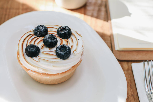Lemon meringue and blueberry tart in white plate on wooden table. Pie Dessert. Horizontal Copy space - Foto, afbeelding