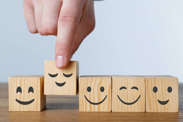 Man arranging cubes with different emoticons in row on wooden table against light background, closeup - Fotó, kép