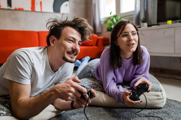 Man and woman lying on the floor at home playing video game console - Fotografie, Obrázek